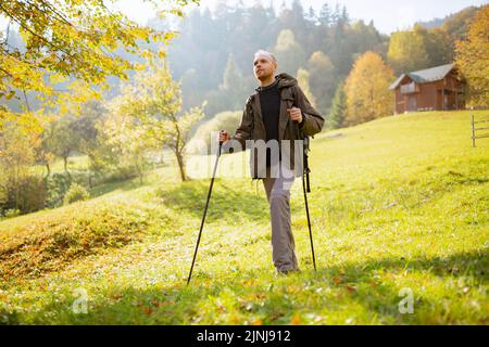 Ritratto di un giovane turista maschile con uno zaino sulle spalle e bastoni da trekking nelle mani. L'uomo viaggia attraverso le montagne, si erge su un mou Foto Stock