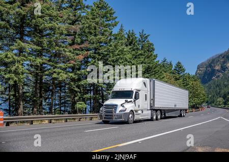 Semirimorchio industriale bianco con cabina a tetto alto per il trasporto di carichi commerciali in semirimorchio più pesante che si sposta lungo l'incredibile strada autostradale Foto Stock
