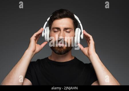 barbuto uomo in cuffie wireless ascoltare musica isolato su grigio, immagine stock Foto Stock