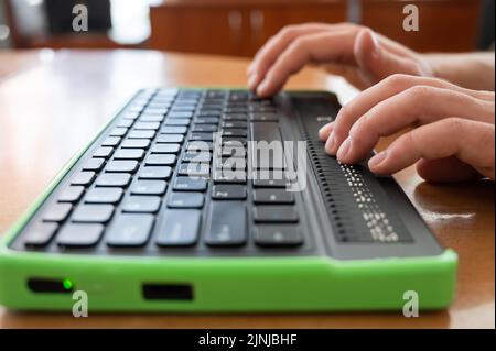 Un uomo cieco utilizza un computer con un display Braille e una tastiera per computer. Dispositivo incluso. Foto Stock