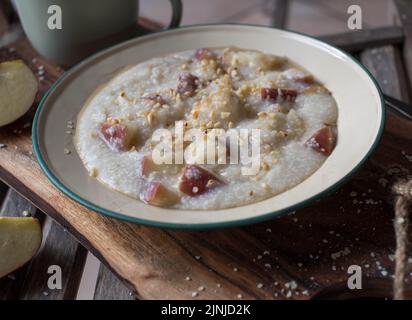 Colazione naturale con porridge di miglio appena cotto, mele, nocciole tostate e sciroppo d'acero. Servito su un piatto di smalto vecchio stile o su una ciotola Foto Stock