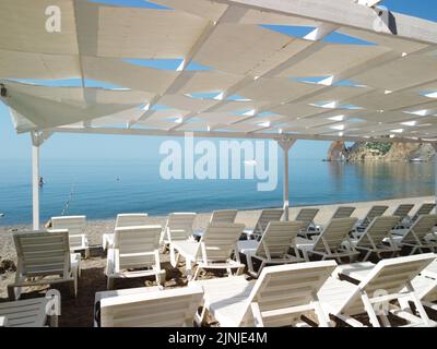 Sedie a sdraio vuote sotto un baldacchino sulla spiaggia. La spiaggia è vuota. Nessuna gente. Lettini in plastica bianca sotto il parasole. La stagione natalizia termina Foto Stock