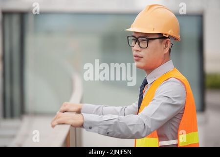 Giovane operaio edilizio asiatico pensivo che ha una breve pausa Foto Stock