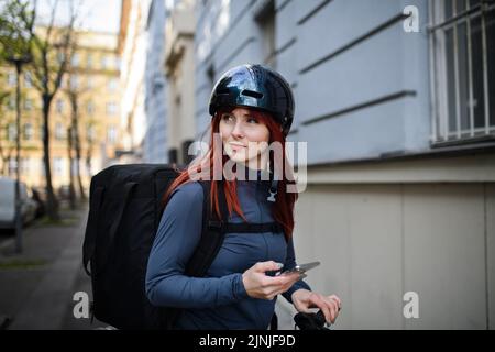 Corriere femminile in bicicletta con zaino termico in arrivo per consegnare cibo ai clienti. Foto Stock