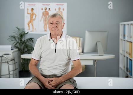 Uomo anziano stanco infelice seduto a letto in ufficio medico Foto Stock