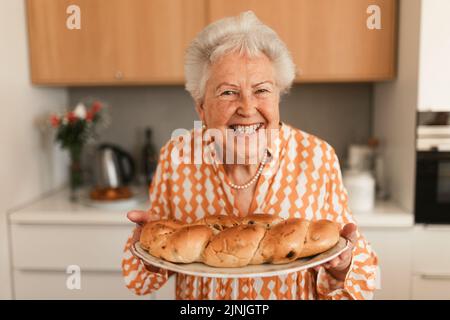 Donna anziana felice con pane dolce intrecciato fatto in casa con uva passa. Foto Stock