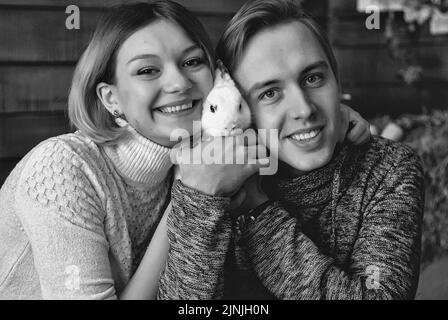 Storia d'amore di giovane felice, divertente coppia in studio, accogliente casa. Coniglio bianco. Decorazioni autunnali, zucche arancioni, foglie. Vacanza in famiglia Foto Stock