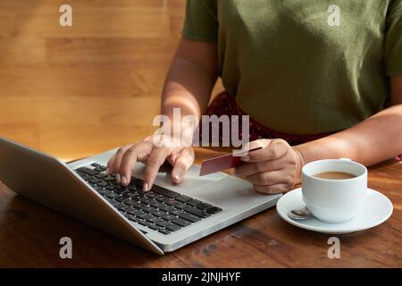 Donna irriconoscibile che indossa una T-shirt a pagamento per il suo ordine online con carta di credito mentre si siede al tavolo del caffè, primo piano Foto Stock