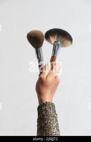 Artista di make-up irriconoscibile che tiene in mano due pennelli mentre si trova su sfondo bianco, primo piano Foto Stock