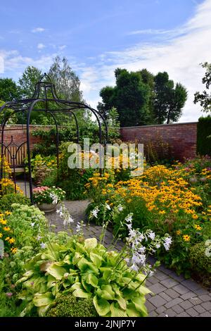 Show Garden, un giardino inglese pieno di fiori estivi fioriti e piante verdi, circondato da un muro di mattoni rossi. Foto Stock