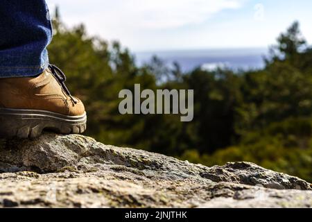 Particolare di una scarpa da uomo arroccata su una roccia di fronte al verde paesaggio montano e al cielo blu. Madrid. Foto Stock
