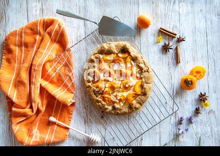 Torta di albicocche con galette posta su fondo di legno con utensili da cucina sul lato Foto Stock