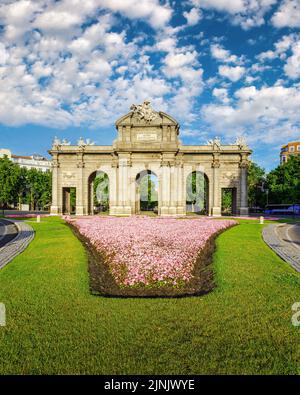 Puerta de Alcala de Madrid in fiori sul terreno e giorno di sole con nuvole bianche. Foto Stock