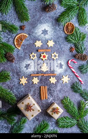 Dolci e biscotti natalizi in forma di albero di natale posto su scrivania grigia con cono di pino e ramo sul lato. Decorazioni invernali e natalizie, ci Foto Stock