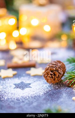 Dolci e biscotti di Natale posti sulla scrivania grigia. Decorazioni invernali, pino e cono. Concetto di natale, regali e vacanze. Luci accese Foto Stock