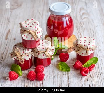 La marmellata di lamponi in piccoli bicchieri è posta su una scrivania di legno. Marmellata fatta in casa di lamponi freschi. Cucina fresca e sana. Foto Stock