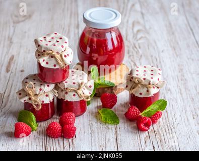 La marmellata di lamponi in piccoli bicchieri è posta su una scrivania di legno. Marmellata fatta in casa di lamponi freschi. Cucina fresca e sana. Foto Stock