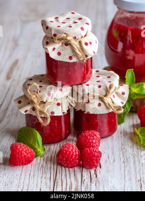 La marmellata di lamponi in piccoli bicchieri è posta su una scrivania di legno. Marmellata fatta in casa di lamponi freschi. Cucina fresca e sana. Foto Stock