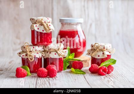 La marmellata di lamponi in piccoli bicchieri è posta su una scrivania di legno. Marmellata fatta in casa di lamponi freschi. Cucina fresca e sana. Foto Stock