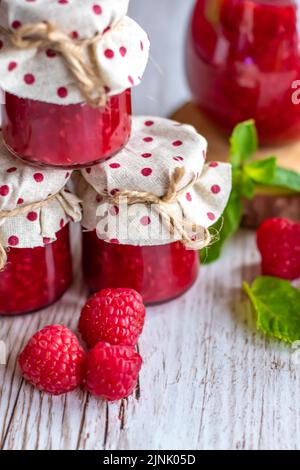 La marmellata di lamponi in piccoli bicchieri è posta su una scrivania di legno. Marmellata fatta in casa di lamponi freschi. Cucina fresca e sana. Foto Stock