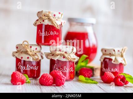 La marmellata di lamponi in piccoli bicchieri è posta su una scrivania di legno. Marmellata fatta in casa di lamponi freschi. Cucina fresca e sana. Traduzione per 'Malina Foto Stock