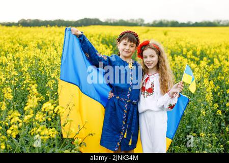 Prega per l'Ucraina. Due ragazze carine che tengono in mano una bandiera nazionale ucraina blu e gialla nel mezzo di un campo di colza Foto Stock