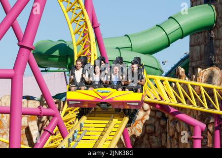 Roller coaster auto con persone felici e spaventato viaggiare lungo la pista verso la fotocamera. Foto Stock