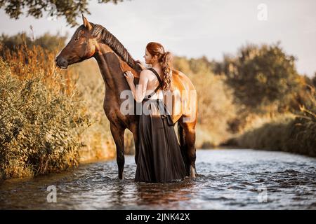 Una donna e un giovane cavallo in piedi in acqua l'uno accanto all'altro godendo l'estate Foto Stock