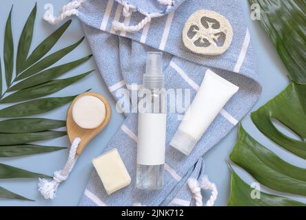 Flacone dispenser spray ricaricabile trasparente e tubo crema bianco su telo da bagno blu vicino agli accessori per la cura del corpo vista dall'alto, spazio copia. Imballo mocku Foto Stock