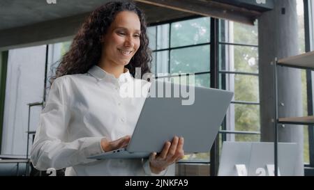 Una donna d'affari di successo che lavora in un ufficio moderno digitando sul laptop comunicare in remoto con il cliente sviluppo progetto scrive e-mail messaggio giovane Foto Stock
