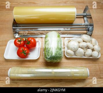 Rotoli di pellicola alimentare in polietilene trasparente per il confezionamento di alimenti su tavola con verdure. Pomodori, funghi e cavolo cinese sono avvolti in Fi cling Foto Stock