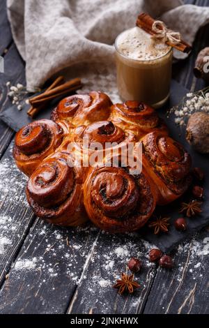 Ciambelle di cannella appena sfornate con spezie e farcitura con bevanda a base di caffè sul tavolo di legno. Foto Stock
