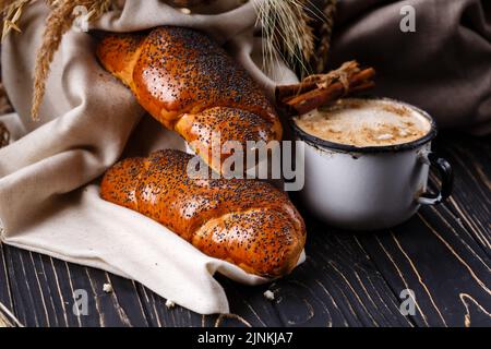 Colazione tradizionale con panini di semi di papavero e caffè su un rustico tavolo di legno scuro. Foto Stock