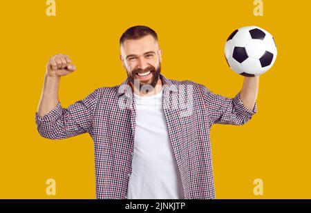 Uomo felice che si diverte alla partita di calcio, tenendo la palla, alzando il pugno, sorridendo e allietando Foto Stock