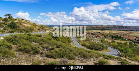 Vista panoramica della strada di montagna con piccolo paese sullo sfondo della valle. Foto Stock