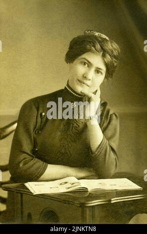 Primo ritratto fotografico vittoriano bianco e nero di giovane donna attraente seduta alla scrivania con libro guardando la fotocamera circa 1895 Foto Stock