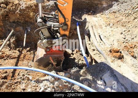 La presa di un escavatore scava terra accanto a un cavo Foto Stock