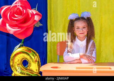 Lysychansk, Ucraina. 1 settembre 2021 - una ragazza con due code di ponytail, archi bianchi e una blusa bianca guarda la macchina fotografica e sorride durante il Foto Stock