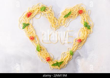 Pasta decorativa a forma di cuore ancora vita formata da pasta ricoperta di pomodori, basilico Foto Stock