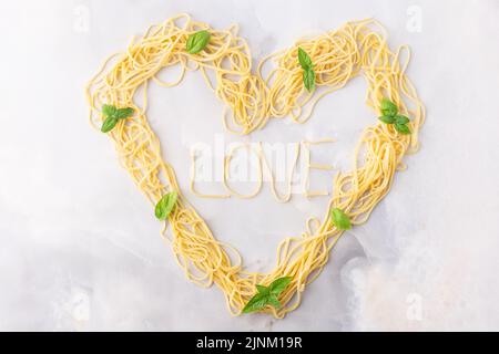 Pasta decorativa a forma di cuore ancora vita formata da pasta ricoperta di pomodori, basilico Foto Stock