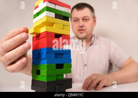 Un uomo gioca a un gioco da tavolo di jenga, tira con attenzione i blocchi multicolore fuori dalla torre. Maggio 22, Zaporozhye, Ucraina Foto Stock