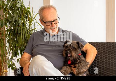 Primo piano di un uomo anziano felice e sorridente (70 anni caucasico) che tiene il suo carino cane Foto Stock