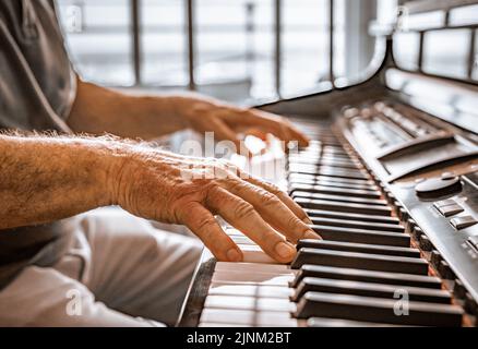 Le mani dell'anziano suonano il pianoforte. Vista ravvicinata della struttura della pelle e dei tasti del piano. Foto Stock