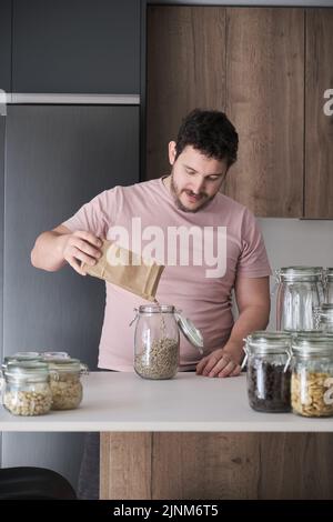 Giovane uomo latino che riempie un vaso con semi di girasole sbucciati da un sacchetto di carta. Foto Stock