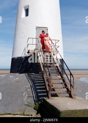Donne elegantemente vestite al Faro di Point of Ayr, aka Talacre Lighthouse, un edificio classificato di II grado situato sulla spiaggia. Galles. Foto Stock