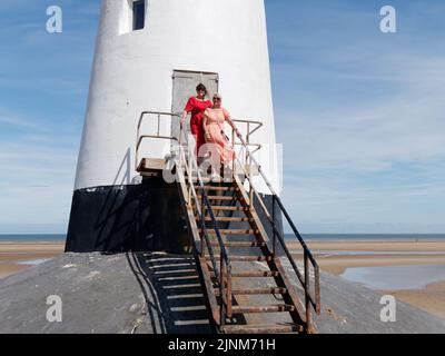 Donne elegantemente vestite al Faro di Point of Ayr, aka Talacre Lighthouse, un edificio classificato di II grado situato sulla spiaggia. Galles. Foto Stock