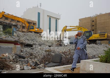 Un uomo pakistano su una chiamata cammina davanti al luogo di demolizione con due escavatori gialli ad al Ghubaiba. Scena diurna all'aperto a Dubai, Emirati Arabi Uniti. Foto Stock