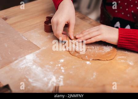 Cottura dei biscotti natalizi. Il bambino decora i biscotti di Natale con la glassa. Stile di vita natalizio stagionale a casa con i bambini. Santa helper. Foto Stock