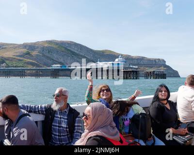 Llandudno, Clwyd, Galles, Agosto 07 2022: Turisti che si godono una gita in barca con il molo e la Grande Orme sullo sfondo Foto Stock