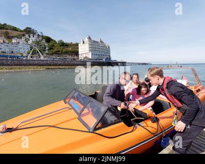 Llandudno, Clwyd, Galles, Agosto 07 2022: I turisti che escono da una barca con la ruota grande e Grand Hotel sullo sfondo. Foto Stock
